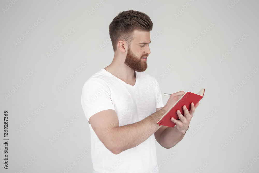 beautiful man with a beard and a fashionable hairstyle dressed in casual clothing standing in profile and seriously recording something in the notebook. stands opposite the white background beautiful man with a beard and a fashionable hairstyle dressed in casual clothing standing in profile and seriously recording something in the notebook. stands opposite the white background