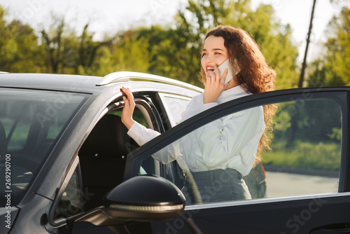Business woman talking on the phone in the parking lot. Stylish young woman standing near the car