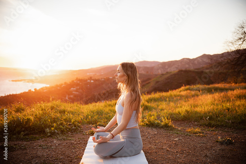 фотографія Side view of sportswoman meditating while sitting on exercise mat against mounta
