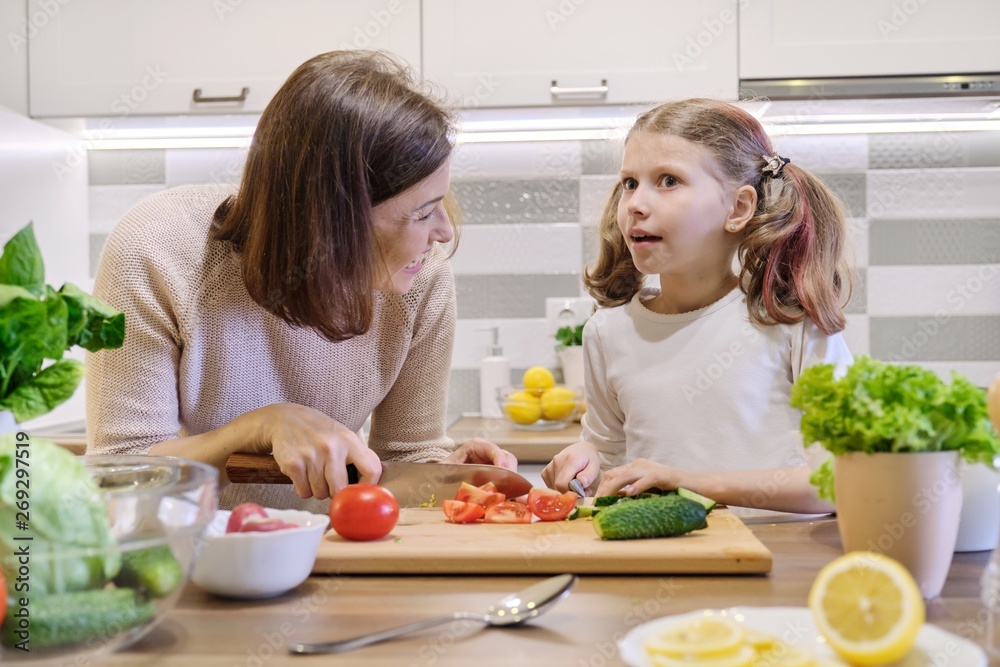 Mother and daughter cooking together in kitchen vegetable salad, parent and child are talking smiling.