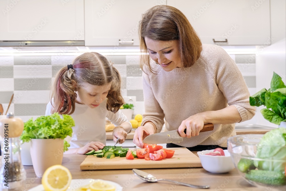 Cooking healthy home meal by family. Mother and daughter cut vegetables at home in the kitchen for salad