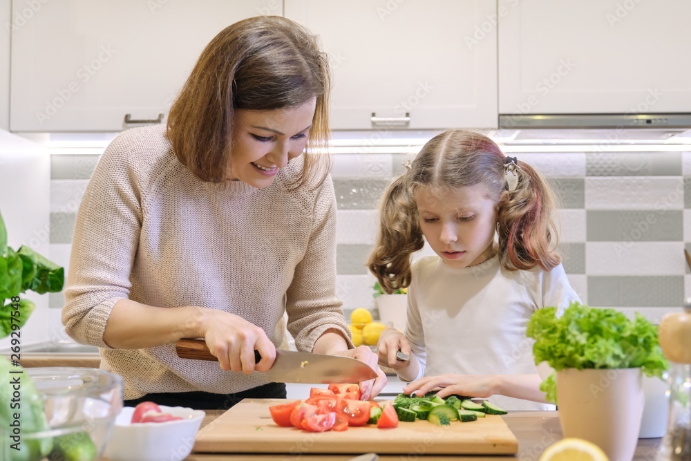 Cooking healthy home meal by family. Mother and daughter cut vegetables at home in the kitchen for salad Cooking healthy home meal by family. Mother and daughter cut vegetables at home in the kitchen for salad
