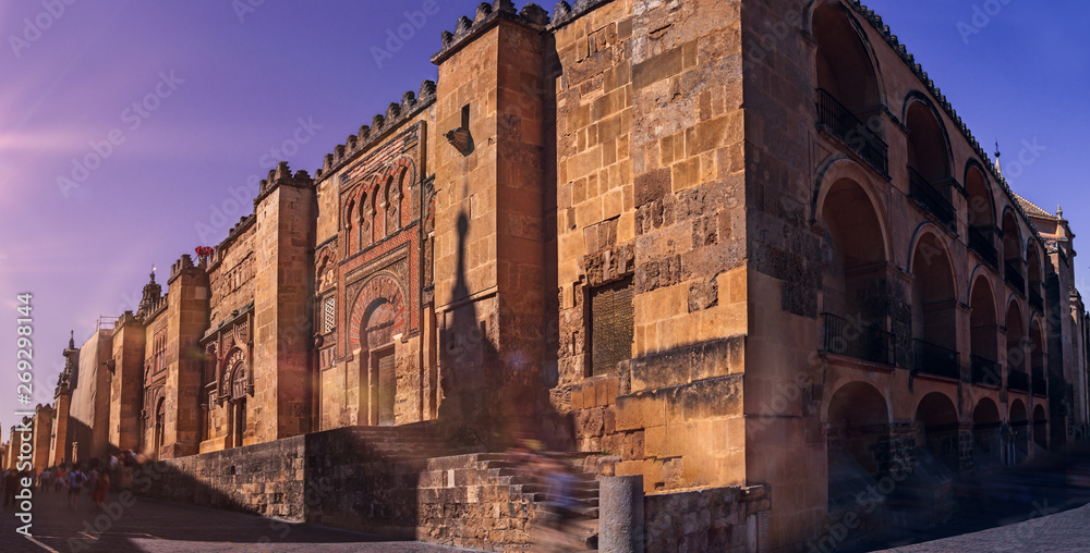 Double page of the outer wall of the Mosque of Cordoba with people out of focus by movement at dusk. Monument in Spain. Concept of culture, travel and tourism