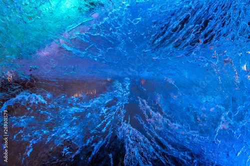 Texture of frozen ice wall illuminated with blue and purple light in background