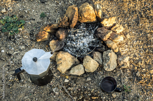 Preparing coffee using a bonfire during a camp in the forest. Bonfire with rocks, coffee maker moka and cup. Preparation of coffee during a trip. photo