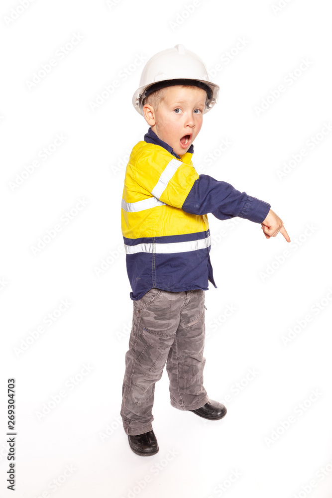 Young blond caucasian boy pointing down with a shocked look role playing a construction worker supervisor in a yellow and blue hi-viz shirt, boots, with white hard hat, minus hammer and tape measure Young blond caucasian boy pointing down with a shocked look role playing a construction worker supervisor in a yellow and blue hi-viz shirt, boots, with white hard hat, minus hammer and tape measure