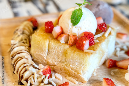 Strawberry honey toast with ice cream on wood plate dish.
