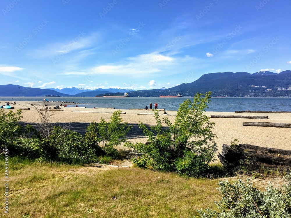 A beautiful view of the sandy beaches of Spanish Banks, with tankers and mountains in the background on a beautiful sunny day.  This is popular spot during the summer in Vancouver, Canada