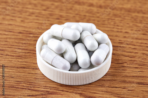 Many white capsules in plastic cap on wooden background