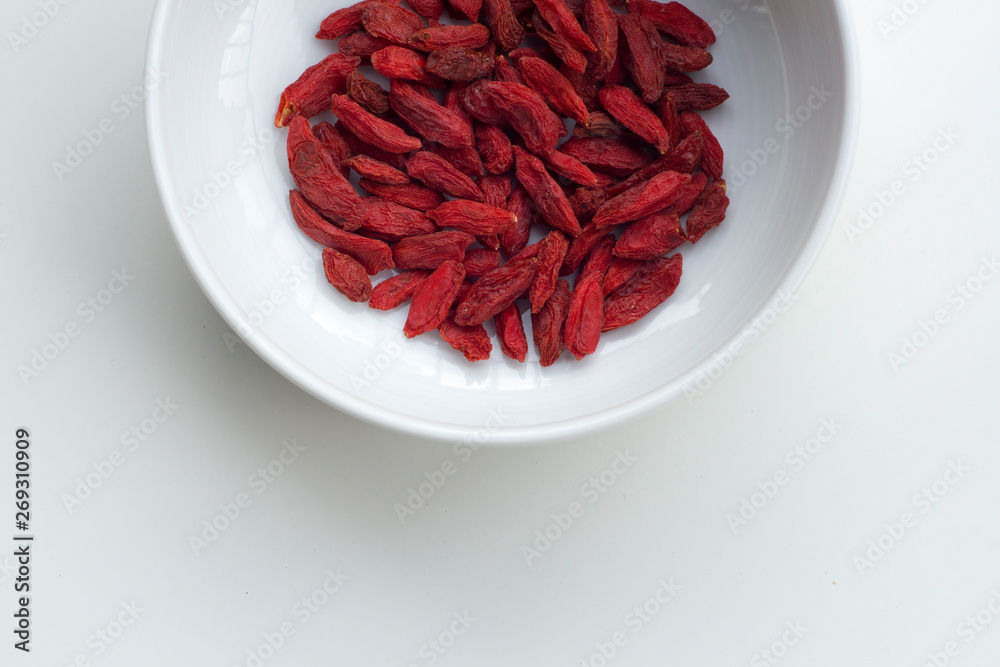 Sun-dried organic goji berries in a white bowl isolated on white background. Sun-dried organic goji berries in a white bowl isolated on white background.