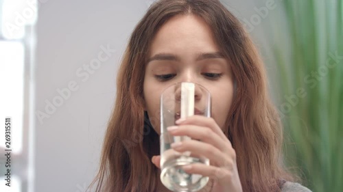 Cheerful woman taking vitamin capsule and drinking water from glass in bath room photo