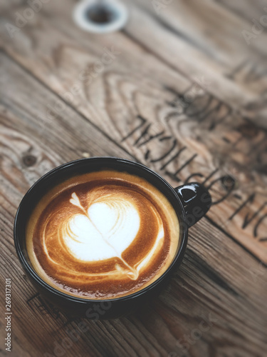 Heart love Latte art coffee in black cup on vintage wooden table. Top view and copy space Dark light and vintage style.