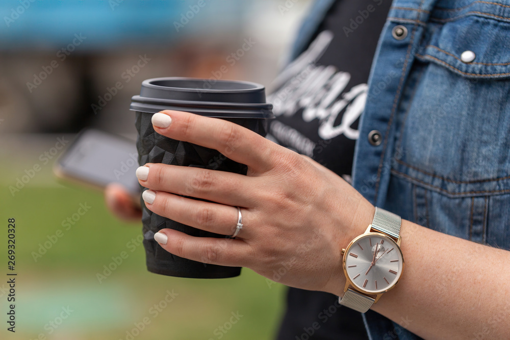 Close up of women's hands holding cell telephone and a cup of coffee