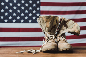 Military boots near American flag with stars and stripes on wooden surface
