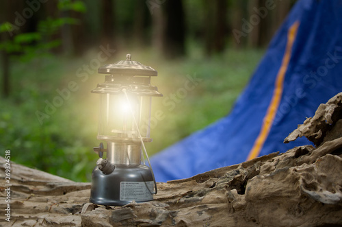 Flashlight vintage old lantern lighting on the wood. Travel camping concept. Burning lantern on a wood at forest in the twilight.