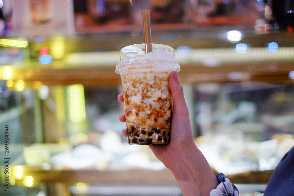 brown sugar bubble milk tea in plastic cup, hand holding a cup of fresh milk ,center focus, bokeh background 