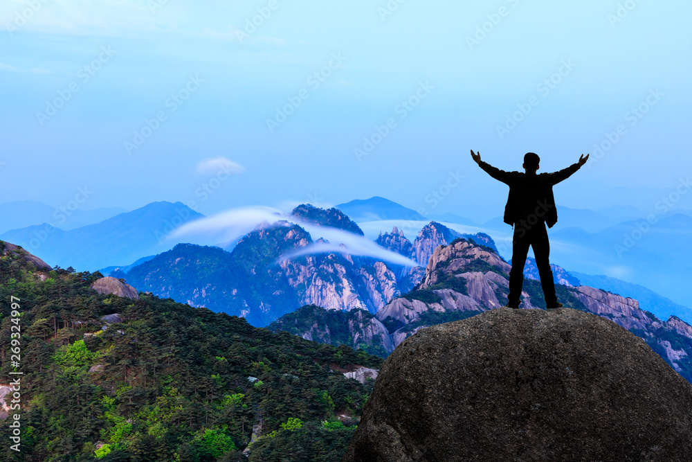 Hiker is standing on a rock with raised hands and enjoying sunrise