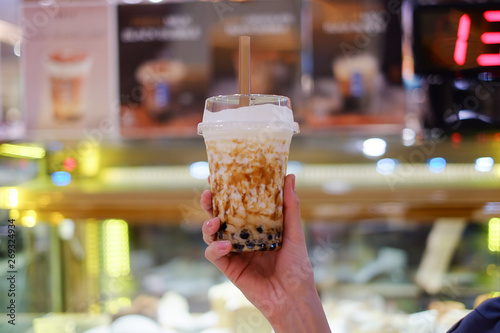 Hand holding a plastic cup of  milk and brown sugar bubble drinks. Center focus. Light Bokeh background , Black Boba