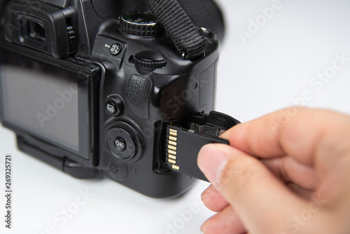 Photographer hand holding SD memory card insert DSLR camera.