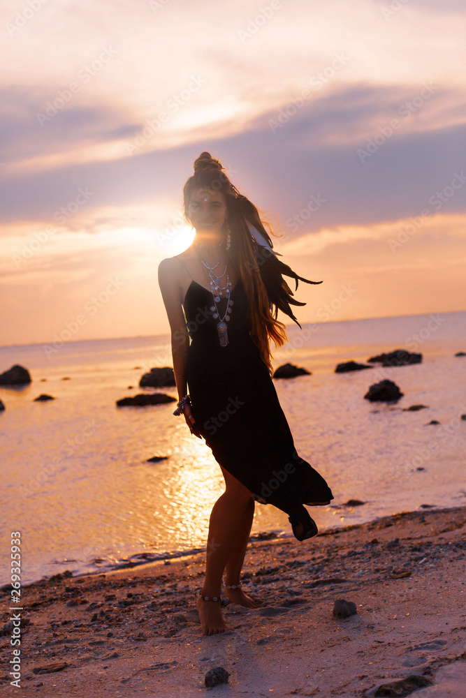 beautiful young boho style woman silhouette on the beach at sunset