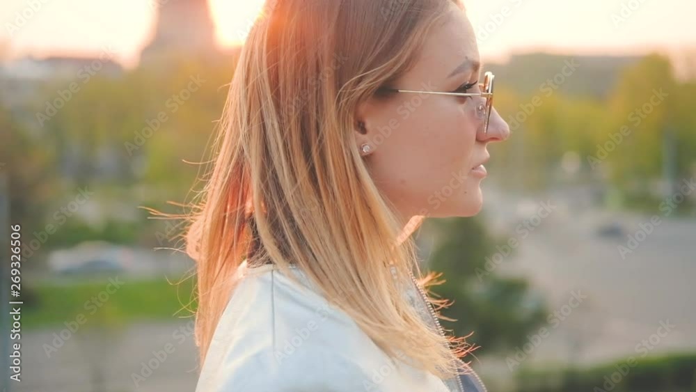 Urban life. Blonde young lady enjoying sunset in city park. Thoughtful facial expression. Blur background. Urban life. Blonde young lady enjoying sunset in city park. Thoughtful facial expression. Blur background.