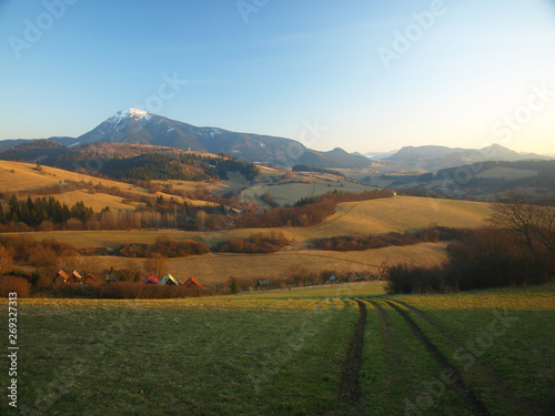 Morning landscape with mountains and blue sky at sunrise with sun reflecting. Evening sunset on the horizon of hills with white snow and green meadow