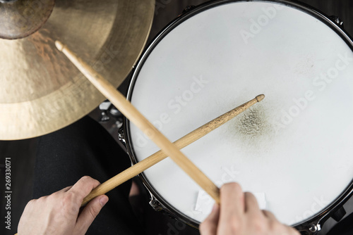 Professional drum set closeup. Man drummer with drumsticks playing drums and cymbals, on black wooden background