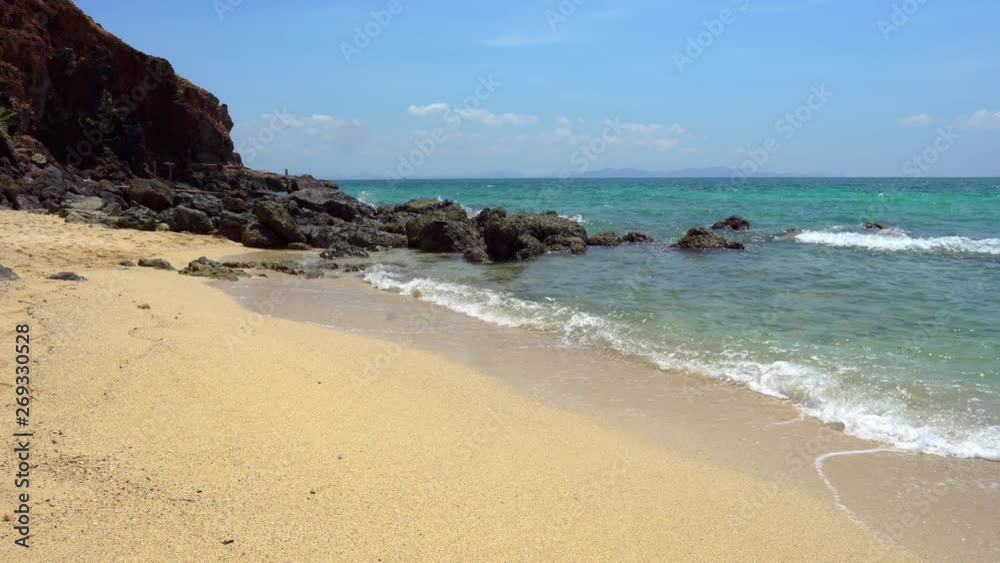 Landscape wide shot of clear blue sea waves rolling and splashing against tropical island rocky sand beach in summer.The sun glimmering sunlight peeking the sea surface with sky and clouds backgrounds Landscape wide shot of clear blue sea waves rolling and splashing against tropical island rocky sand beach in summer.The sun glimmering sunlight peeking the sea surface with sky and clouds backgrounds