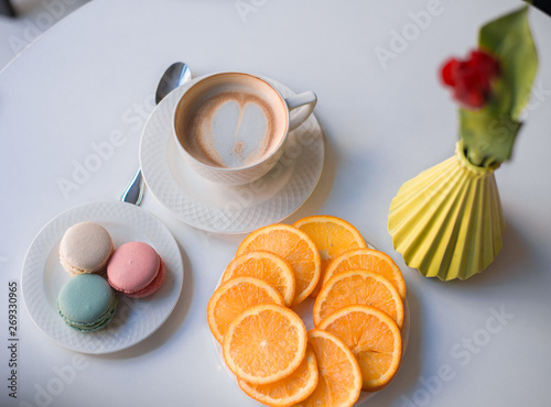 Morning coffee with macaroons and orange on the table with flower