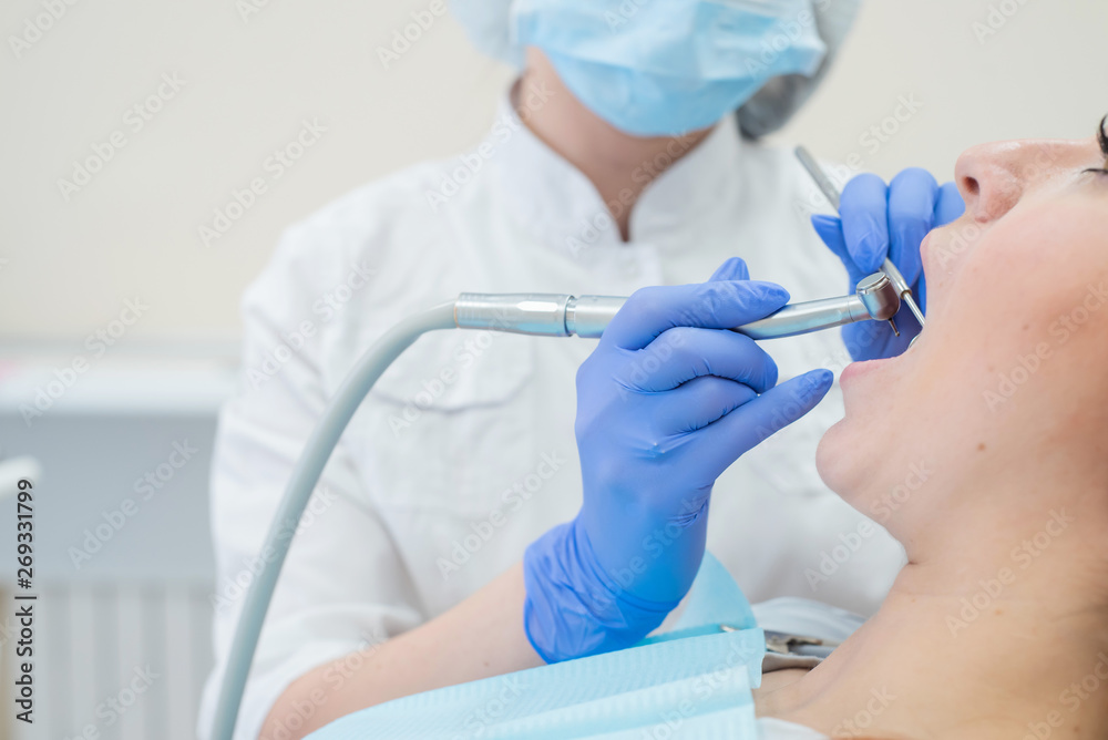 An attractive smiling female doctor in white uniform examines a red-haired female patient. Dentist produces treats teeth with a drill. Close-up An attractive smiling female doctor in white uniform examines a red-haired female patient. Dentist produces treats teeth with a drill. Close-up