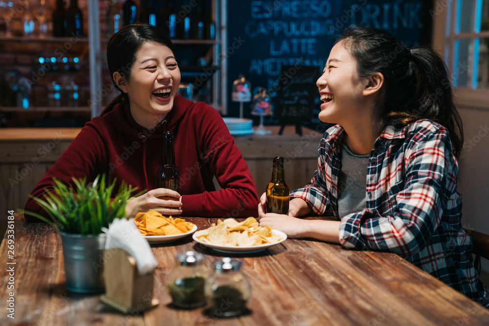 Friends in cafe pub at night drinking beer talking having fun. two asian women sisters enjoy single last day in bar eating chips laughing chatting. happy college girls friends celebrating graduation. Friends in cafe pub at night drinking beer talking having fun. two asian women sisters enjoy single last day in bar eating chips laughing chatting. happy college girls friends celebrating graduation.