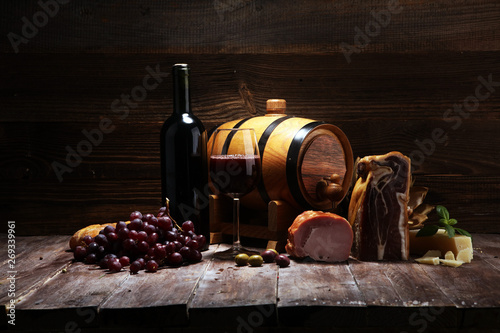 Fototapeta Naklejka Na Ścianę i Meble -  Still life in a rustic style. Grapes on a wooden table with a bottle of wine and meat and cheese. Antipasto and red wine
