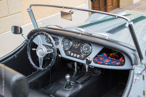 View of the interior of a classic convertible car, with a metallic steering wheel and the dashboard