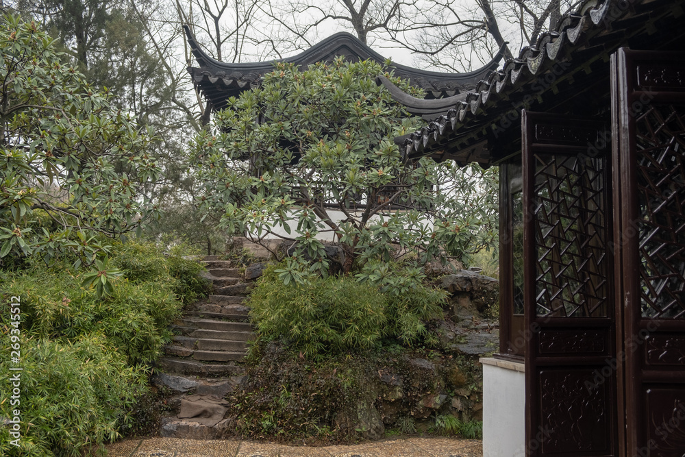 China, Suzhou, Humble Government Park pavilion with red wood columns and black roof on the hill with stairs hidden in trees China, Suzhou, Humble Government Park pavilion with red wood columns and black roof on the hill with stairs hidden in trees
