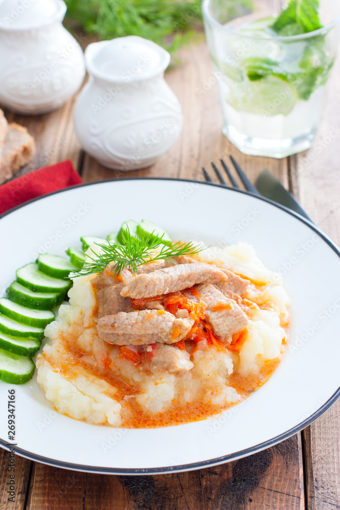 Pork with gravy and mashed potatoes and fresh cucumber on a wooden table, selective focus Pork with gravy and mashed potatoes and fresh cucumber on a wooden table, selective focus