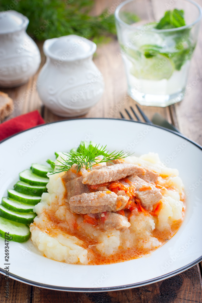 Pork with gravy and mashed potatoes and fresh cucumber on a wooden table, selective focus Pork with gravy and mashed potatoes and fresh cucumber on a wooden table, selective focus
