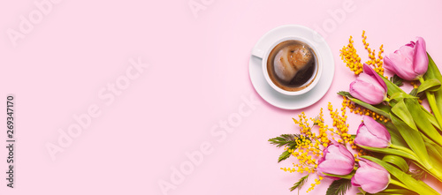 Pink tulips and mimosa flowers with cup of coffee on pink background.