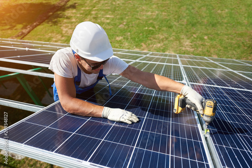 Professional worker installing solar panels on the green metal construction, using different equipment, wearing helmet. Innovative solution for energy solving. Use renewable resources. Green energy.
