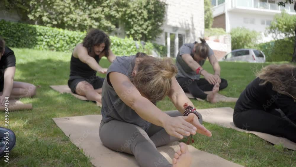 Yoga group stretching on mats in park. Flexible men and women sitting on yoga mats and training outdoor. Yoga concept Yoga group stretching on mats in park. Flexible men and women sitting on yoga mats and training outdoor. Yoga concept