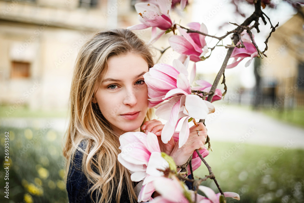 Fototapeta premium Blonde woman posing with magnolia in bloom looking in camera.