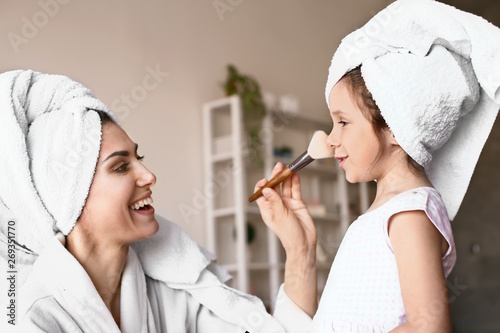 Mother with cute daughter doing makeup at home