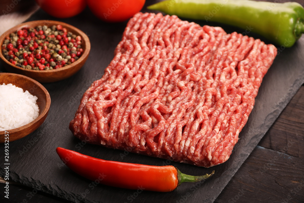 raw minced meat on plate, ingredients for burger with tomato, pepper, onion, spices and seasonings on black background. raw minced meat on plate, ingredients for burger with tomato, pepper, onion, spices and seasonings on black background.