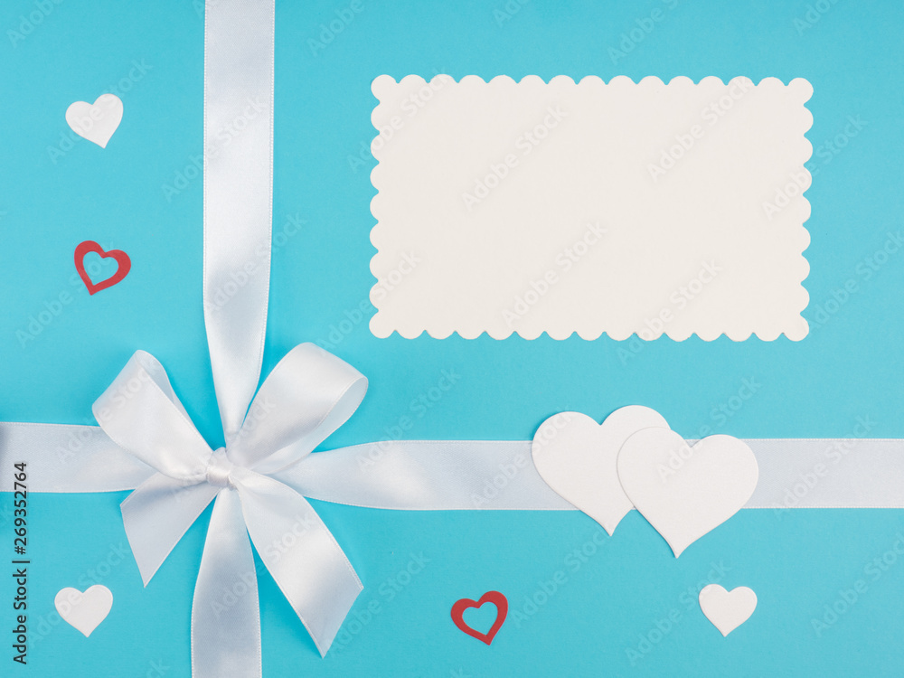 White satin ribbon with bow, red and white hearts on blue background with copy space. Greeting card concept