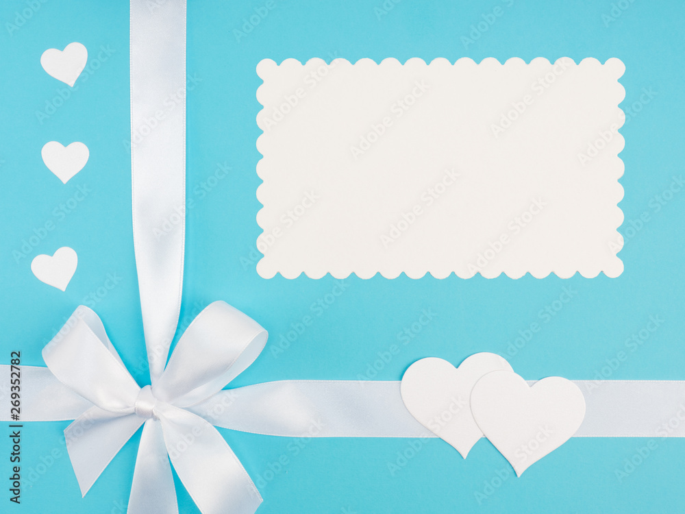 White satin ribbon with bow, white hearts on blue background with copy space. Greeting card concept