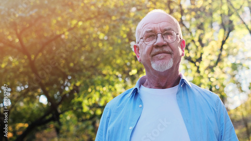 Portrait of senior man with a beard smiling while standing outside in sunlight.