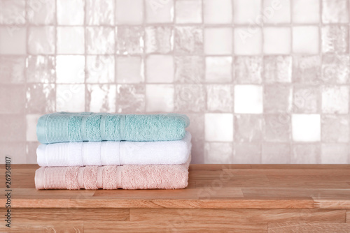 Bath towel pile on wooden surface before ceramic tile wall