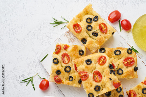 Sliced pieces of focaccia with tomatoes, olives and rosemary. Copy space for text. Traditional Italian flat bread. Top view.
