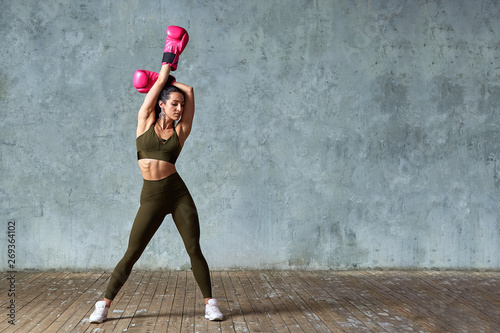 Beautiful athletic girl posing in pink boxing gloves on a gray background. Copy space. Concept sport, fight, goal achievement.