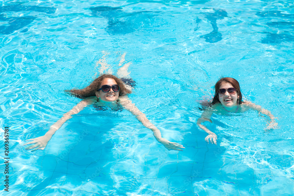 Two brunette girls swim on vacation in the pool