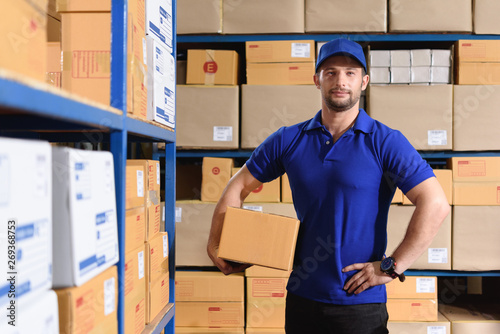 Portrait of delivery staff in blue uniform stand in warehouse hold a parcel box photo